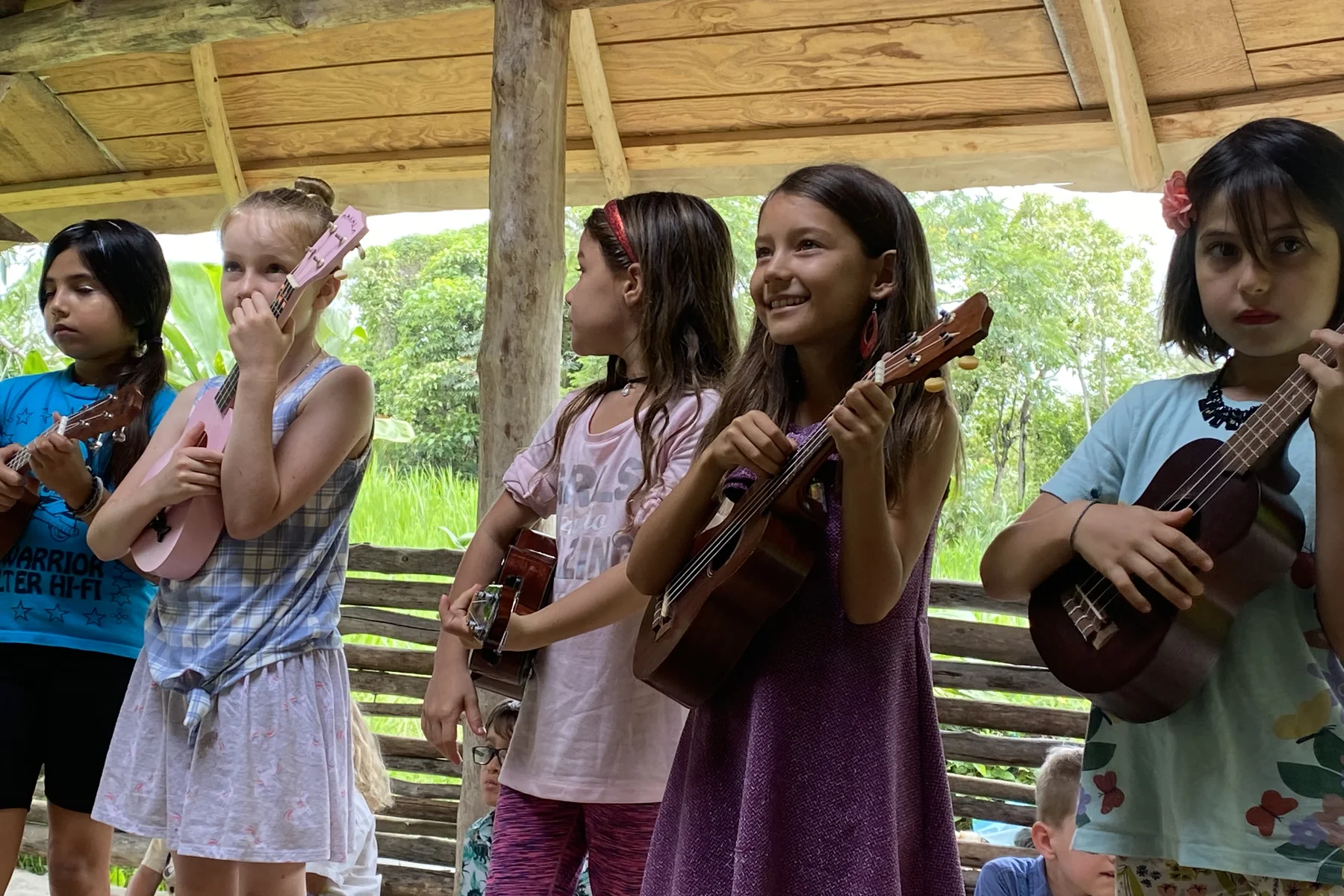 Young musicians sharing ukulele and song under a community shelter